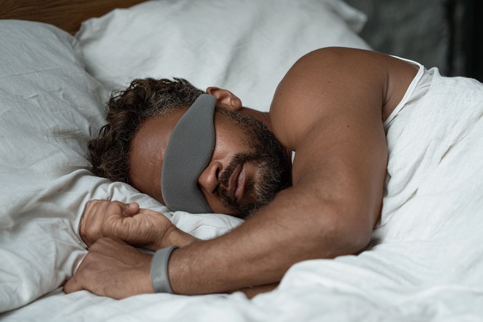 Man sleeping peacefully in bed wearing Restora Dream Smart Sleep Band to track deep and REM sleep