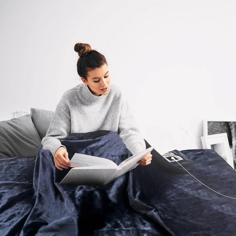 Woman relaxing with a grounding blanket, reading in a cozy setting