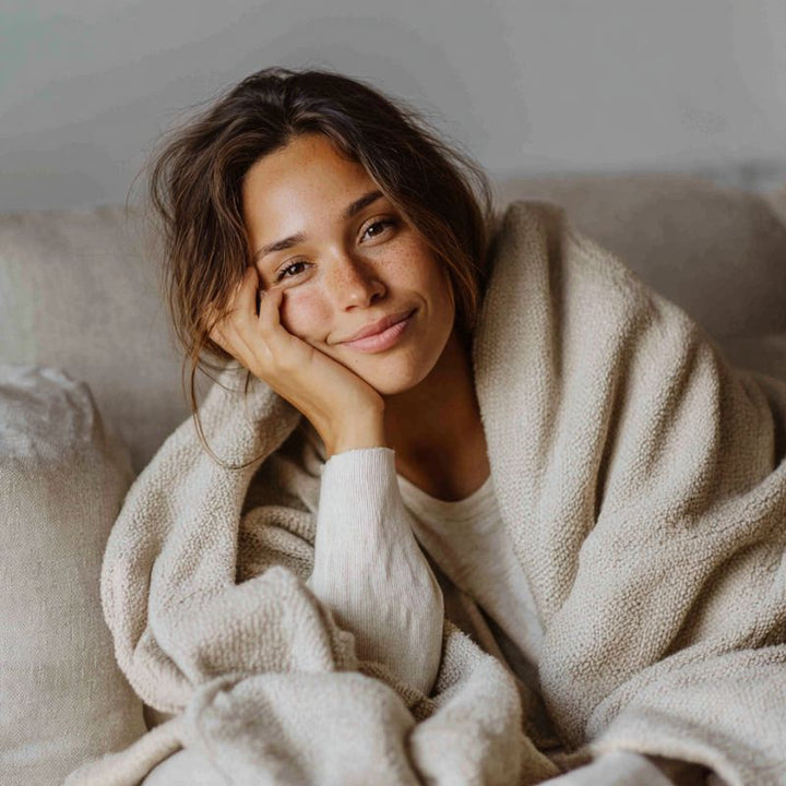 Woman wrapped in a grounding blanket on a couch, smiling.